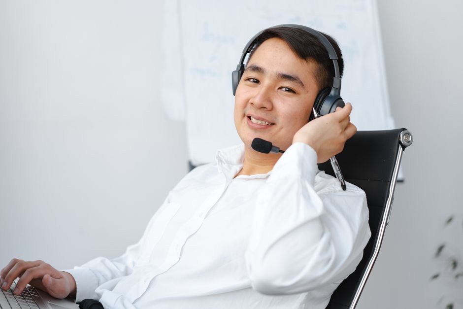 Agente de call center asiático sentado à mesa com fone de ouvido, sorrindo.