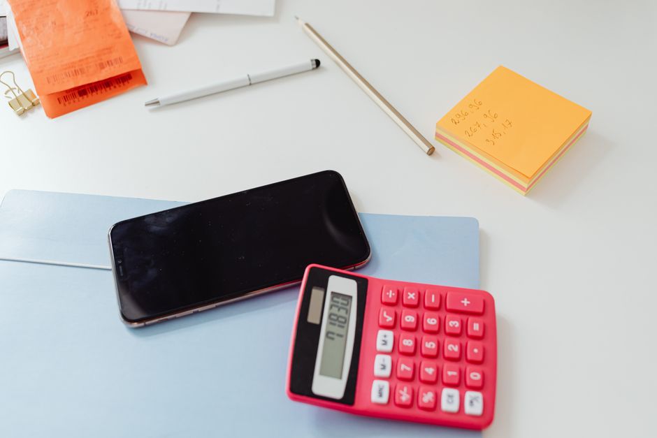 Uma mesa de escritório organizada com uma calculadora, smartphone e post-its em uma superfície branca.