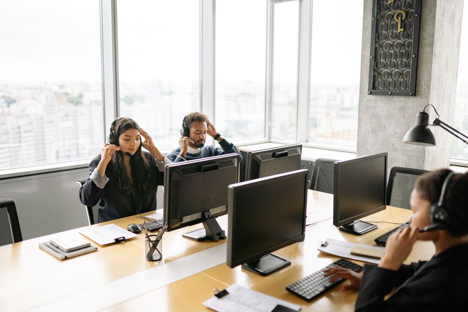 Agentes de call center focados trabalhando em computadores com fones de ouvido em um ambiente de escritório iluminado.