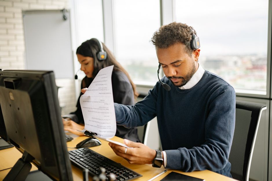 Agentes de call center com headsets trabalhando em um escritório moderno, revisando documentos.