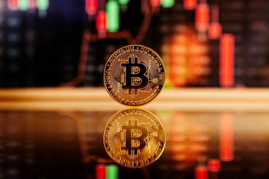 Close-up de uma moeda Bitcoin com um gráfico de mercado de ações ao fundo, simbolizando o comércio de criptomoedas.
