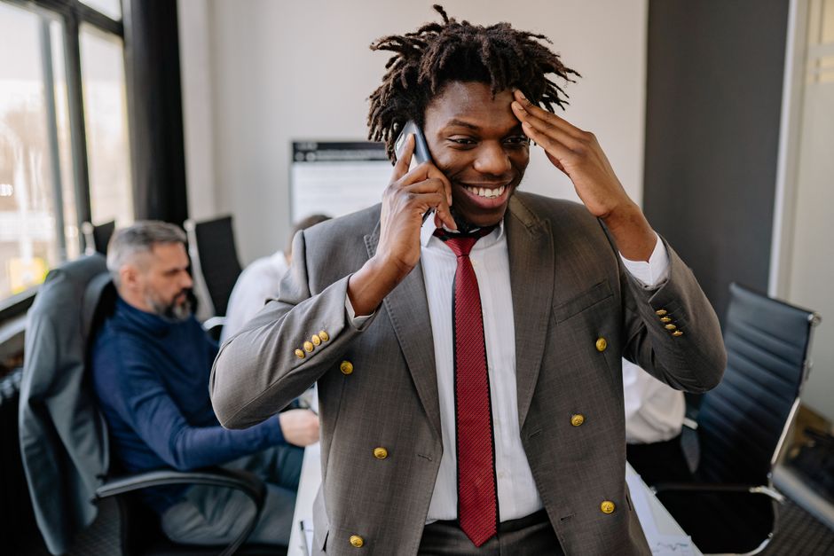 Empresário sorridente com dreads no escritório, falando ao telefone.