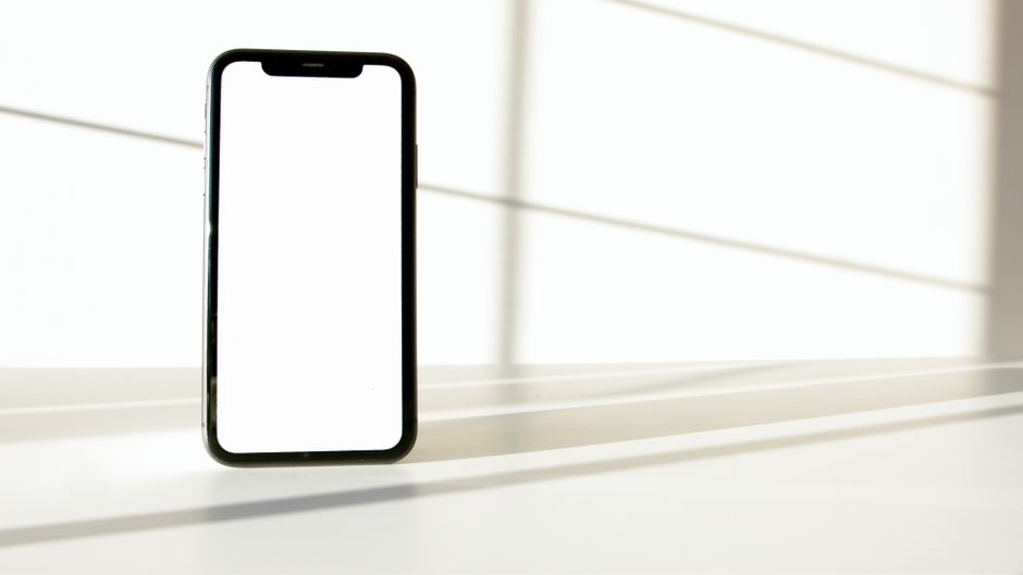 Um smartphone elegante exibido sobre uma superfície branca com contraste dramático de luz e sombra.