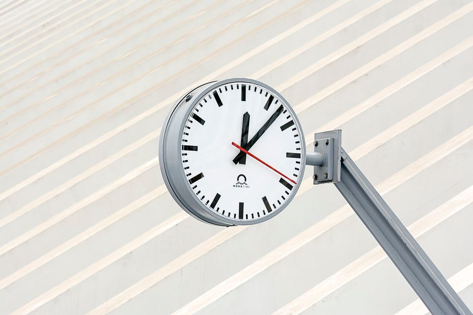 Close-up de um relógio moderno com design minimalista contra um fundo listrado.