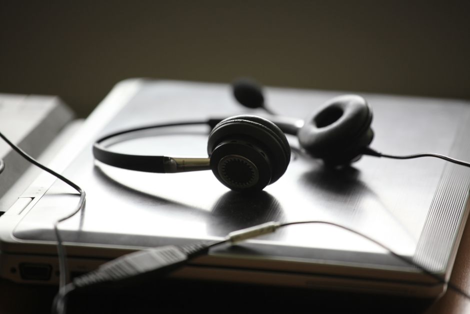 Fone de ouvido preto sobre um laptop prata fechado, simbolizando trabalho remoto ou comunicação digital.